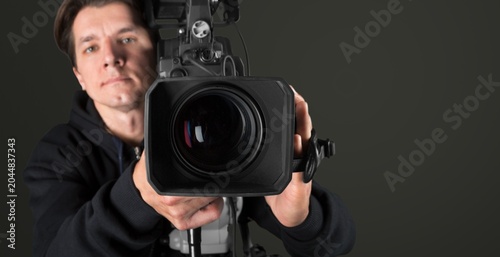 Male videographer operating professional video camera in studio on dark background