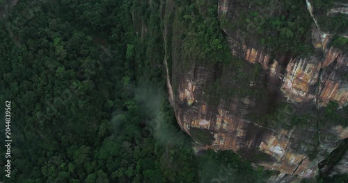 Drone flying near steep cliff with dense fog and deep valley below