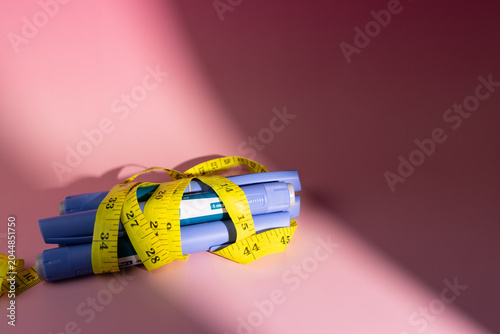 Semaglutide glp1 injector pens wrapped in a yellow measuring tape for type 2 diabetes management and obesity on pink background.