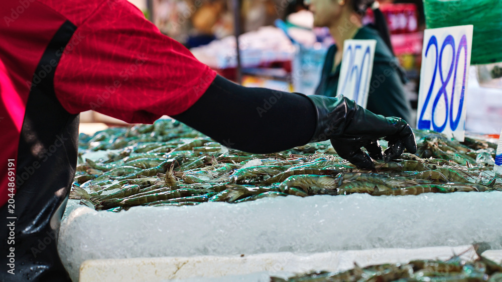 Obraz premium Fishmonger sorting fresh prawns on ice at traditional seafood market in Thailand