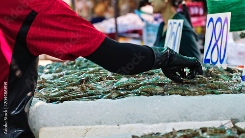 Bild auf Leinwand Fishmonger sorting fresh prawns on ice at traditional seafood market in Thailand