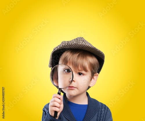 Tableau sur toile Little boy in flat cap looking through magnifying glass over yellow background