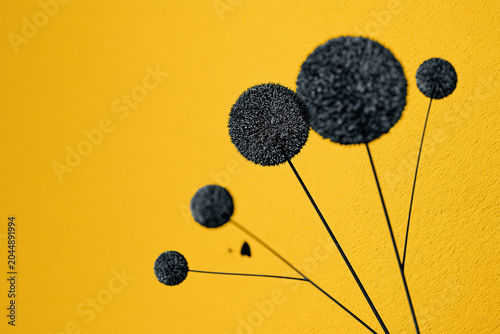 Black round shapes on thin sticks against a bright yellow wall create a striking visual effect in a modern space