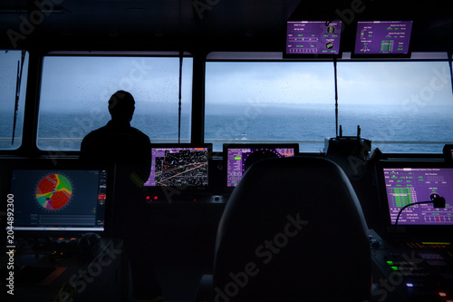 Officer on navigational watch in container ship's bridge at dusk