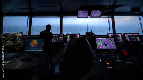 Officer on navigational watch in container ship's bridge at dusk