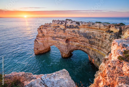 Sunrise at Praia da Marinha beach in Algarve, Portugal, with ocean cliffs, sea stacks and bright clouds over the sea.