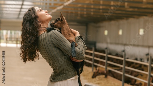 Canvastavla Young woman tenderly holding a baby goat in a barn with other animals