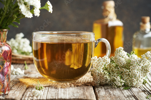 A cup of herbal tea with fresh yarrow flowers on a wooden table