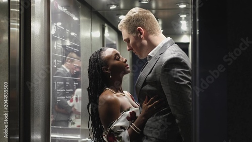 Bild auf Leinwand A handsome young man and a beautiful woman look at each other and smile while standing in an elevator