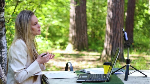 A charming woman conducts an insightful online consultation in the embrace of nature. Her warm demeanor and expert guidance create a memorable atmosphere for all involved. Slow motion 4k video.