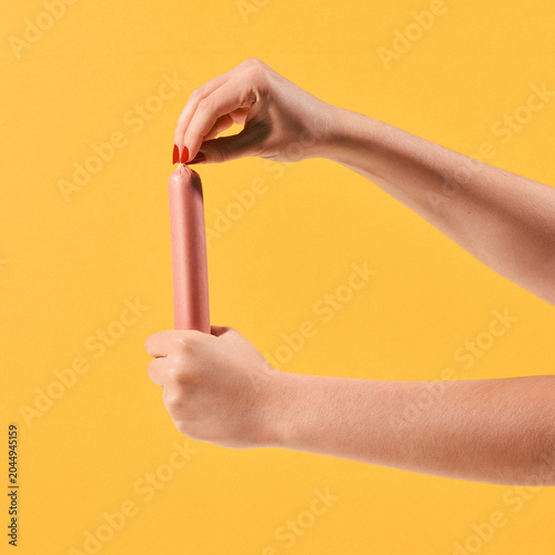 Female Hands Holding Sausage on Yellow Background