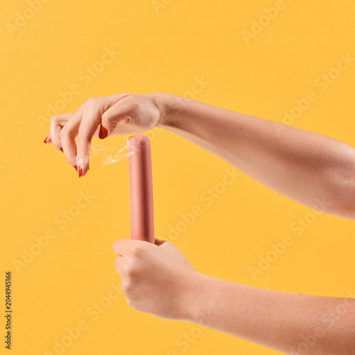 Female Hands Holding Sausage on Yellow Background