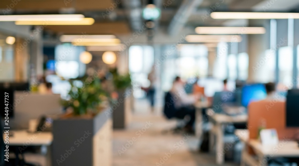 Fototapeta premium Blurred open plan office interior background with desk workstations and soft warm ambient lighting
