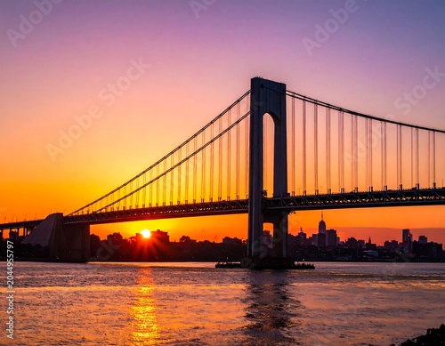 Dramatic Suspension Bridge Silhouette at Sunset Over Calm River and City Skyline