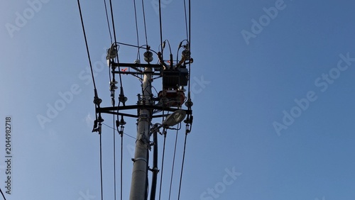 Concrete power pole with electrical wires, insulators, equipment against clear blue sky. Power distribution grid infrastructure. Concept of electricity network, public utilities, energy supply 