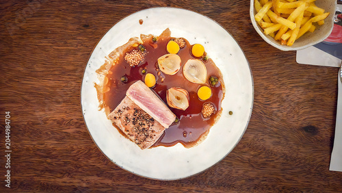 Seared tuna steak with sauce and pearl onions on restaurant plate
