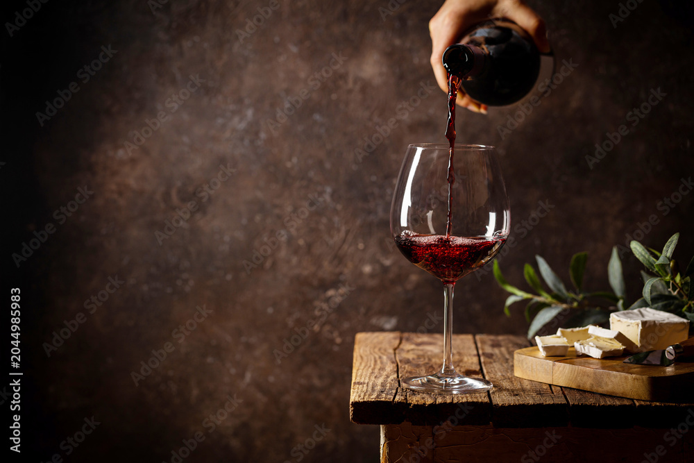 Fototapeta premium Pouring red wine into the glass against rustic dark wooden background