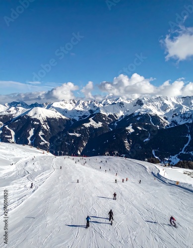 Snow Covered Skiers Descending Wide Alpine Slope Beneath Mountain Range
