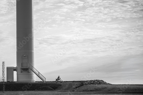Wind turbine. Black and white minimalist shot of a cyclist riding past a massive wind turbine base.