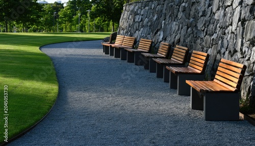 Serene park pathway lined with empty benches against a rustic stone wall