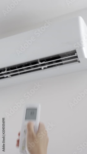 Hand using remote control to adjust temperature on wall mounted air conditioner in modern room. Concept of home cooling, indoor climate control and summer comfort
