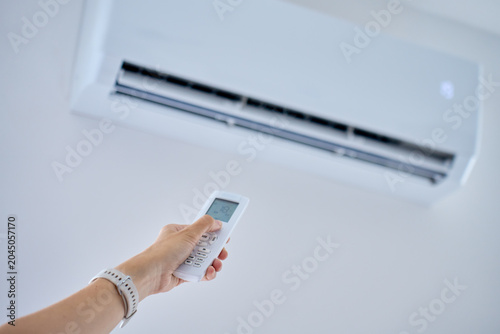 Hand adjusts a wall air conditioner with a remote control in a bright room. Concept of cooling, temperature setting and climate control.