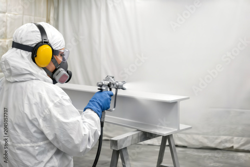 Worker in protective suit spray painting a steel beam in industrial facility.