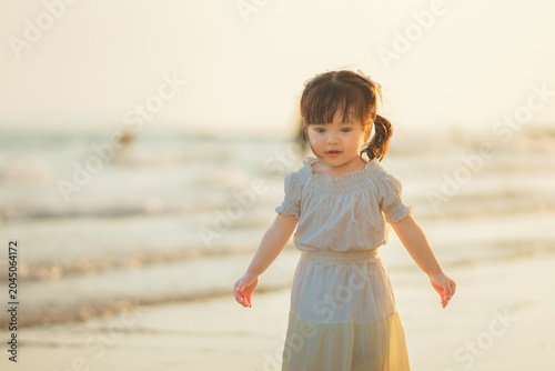 Cute little Asian girl walking on sandy beach at sunset, happy child enjoying tropical sea view during golden hour, family travel vacation, outdoor learning, active childhood growth and parenting