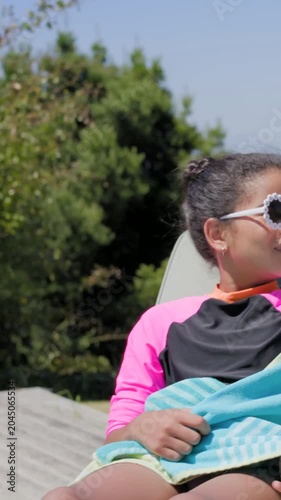 Vertical video: Talking mom in coral top on deck, panning showing daughter in flower shades, towel