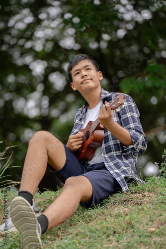 The boy is playing the ukulele on the lawn in the park.