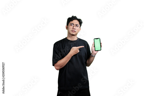 A young Asian man holding a smartphone with a green screen mockup while smiling at the camera. Isolated on a light gray background with copy space. Concept of mobile application promotion, digital mar