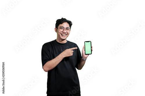 A young Asian man holding a smartphone with a green screen mockup while smiling at the camera. Isolated on a light gray background with copy space. Concept of mobile application promotion, digital mar