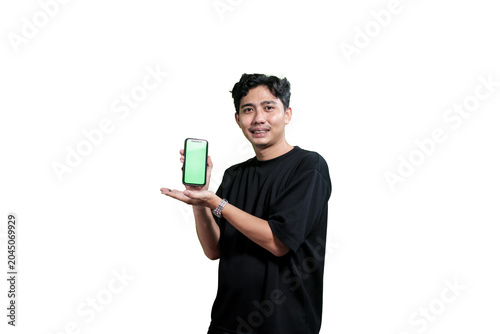 A young Asian man holding a smartphone with a green screen mockup while smiling at the camera. Isolated on a light gray background with copy space. Concept of mobile application promotion, digital mar