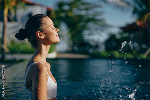 Принти на полотні A woman at a sunlit poolside, eyes closed, enjoying a breezy outdoor moment as w