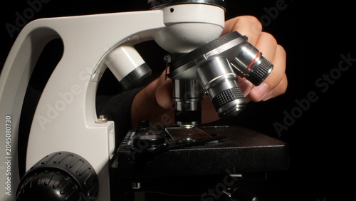 Foto Hand adjusting microscope objectives and stage to focus on a slide in a dark lab