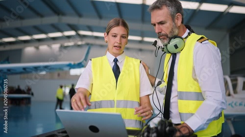 Pilot and engineer discussing flight plan on laptop in hangar