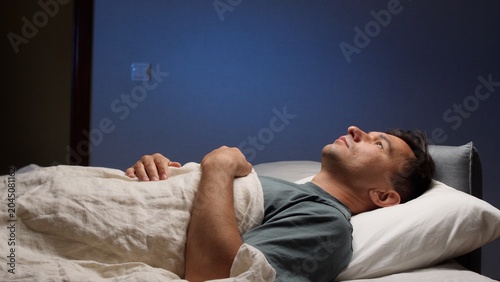 Obraz na płótnie Man lying awake in bed at night, staring at the ceiling, struggling with insomni