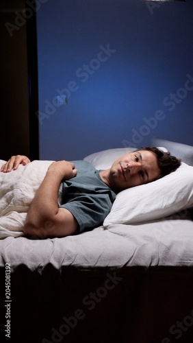 Foto Young man lies awake in bed at night, staring into the darkness with worried, pe