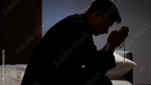 Bild auf Leinwand Man holding rosary beads, with hands clasped, bowing head in deep prayer and sin