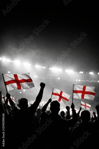 England Fans Silhouetted With England Flags In Black And White Stadium Crowd, England Supporters Cheering Under Bright Match Lights At Night. Football Fans. Soccer, Football World Cup Concept.