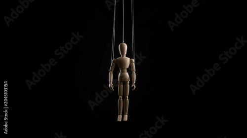 Articulated wooden mannequin puppet hanging by strings against a solid black background, concept of manipulation and control. Dark psychological theme, theatrical drama.