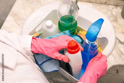 Hands in pink gloves handle cleaning supplies by a sink