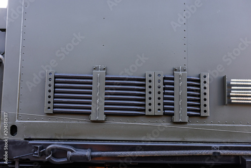 Military equipment and army equipment.. Olive drab military vehicle side panel showing secured tool racks, riveted armor plates, mounting brackets, weathered paint and gritty industrial
