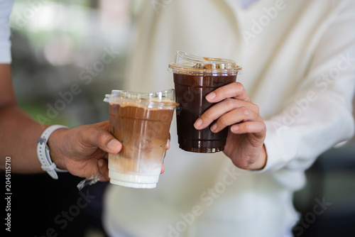 Hands of woman and man holding glass of ice coffee together at cafe.