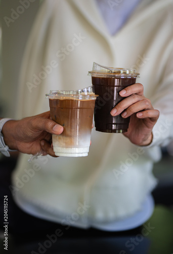 Hands of woman and man holding glass of ice coffee together at cafe.