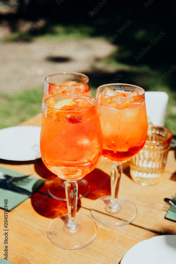 Fototapeta premium Three orange drinks with ice on a wooden table outdoors