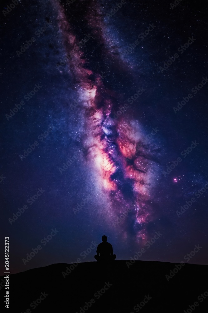 Fototapeta premium Man sits in meditation silhouette under bright Milky Way galaxy. Contemplating cosmos, universe, night sky, celestial wonders, inner peace, spiritual connection, solitude. Serenity under stars.