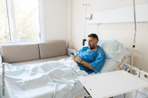 Fotografía Male patient using smartphone recovering in hospital bed