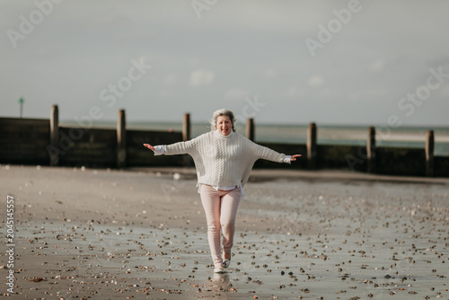 Fotografía Joyful mature woman walking freely on beach with arms outstretched in happiness