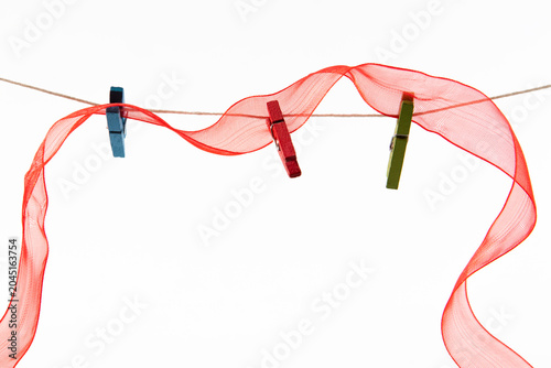 A wavy red mesh ribbon pinned to a thin jute twine rope with three colorful wooden clothespins against a clean white background